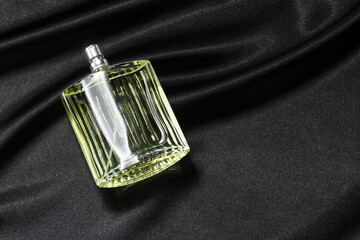 Luxury men's perfume in bottle on black satin fabric, space for text