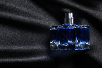 Luxury men's perfume in bottle on black satin fabric, top view. Space for text