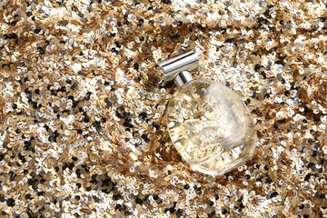 Luxury perfume in bottle on fabric with golden sequins, above view
