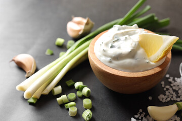 Delicious yogurt in bowl, green onion, garlic and salt on black table, closeup