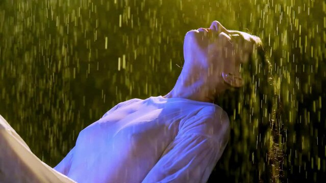 Delighted lady incurves enjoying moisture of studio rain. Young woman with red lipstick has fun holding on person under falling water drops slow motion