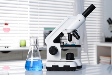 Laboratory analysis. Flask with blue liquid and microscope on white table indoors