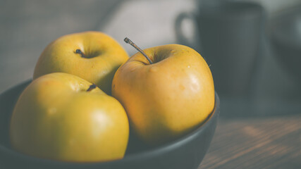 Yellow apples in a clay brown plate on the kitchen table