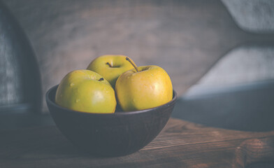 Yellow apples in a clay brown plate on the table