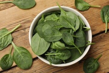 Fresh spinach leaves in bowl on wooden table, flat lay