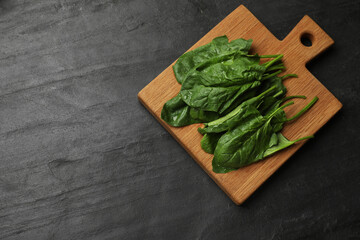 Board with wet fresh spinach leaves on dark textured table, top view. Space for text