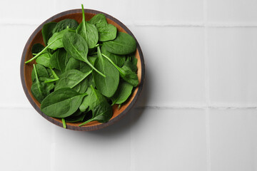 Fresh spinach leaves in bowl on white tiled table, top view. Space for text
