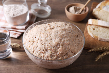 Fresh sourdough in bowl, water, spikes and bread on wooden table, closeup