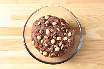 Raw chocolate dough with nuts in bowl on wooden table, top view