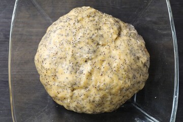 Raw dough with poppy seeds in bowl on black wooden table, top view