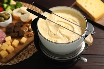 Fondue with tasty melted cheese, forks and different snacks on wooden table