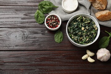 Tasty spinach dip with egg in bowl, spices and bread on wooden table, flat lay. Space for text