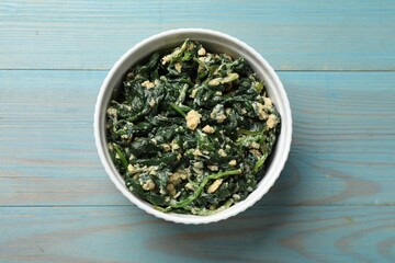 Tasty spinach dip with egg in bowl on light blue wooden table, top view