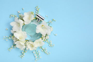 Luxury perfume and floral decor on light blue background, flat lay. Space for text