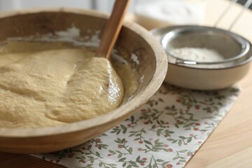 Raw dough in bowl on wooden table, closeup