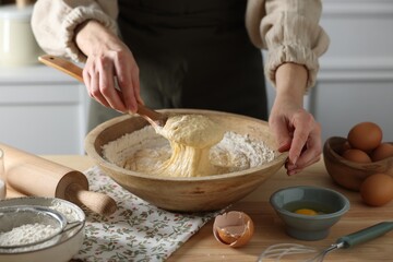 Woman kneading dough with spoon in bowl at wooden table indoors, closeup