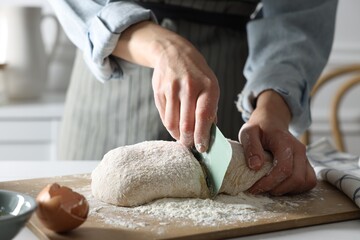 Woman cutting dough at white wooden table in kitchen, closeup