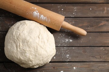 Raw dough and rolling pin on wooden table, top view. Space for text