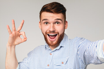 Happy millennial guy showing OK sign on camera