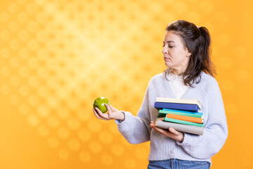 Woman with stack of books in hands enjoying fresh apple, living healthy, isolated over studio...