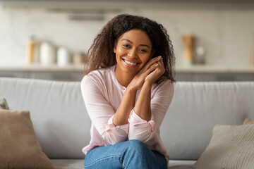 Positive young black woman sitting on couch at home