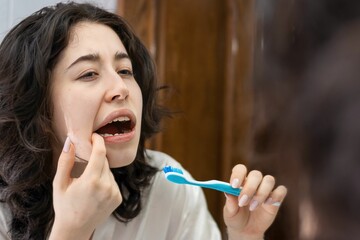 portrait of a latin woman holding a toothbrush looking at her molars and teeth in the mirror. oral hygiene problems in young people is very common