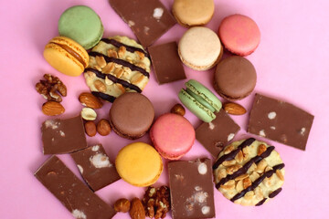 Pastel macarons, almond chocolate, peanut butter cookies and various nuts on bright pink background. Selective focus.