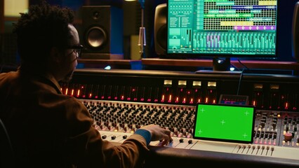 Sound engineer expert recording audio tracks next to tablet mockup, adding sound effects on songs with mixing console. Producer pressing buttons and sliders in control room. Camera B.