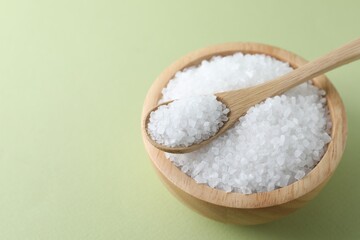 Organic white salt in bowl and spoon on olive background, closeup. Space for text
