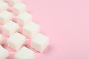 White sugar cubes on pink background, closeup. Space for text
