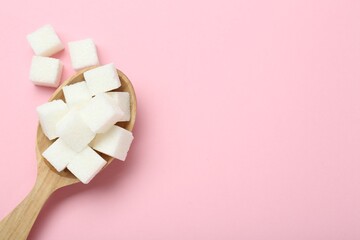 White sugar cubes in wooden spoon on pink background, top view. Space for text