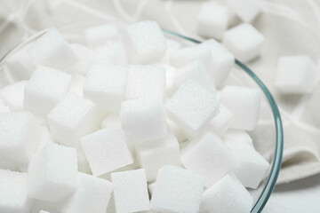 Many sugar cubes in glass bowl on white wooden table, closeup