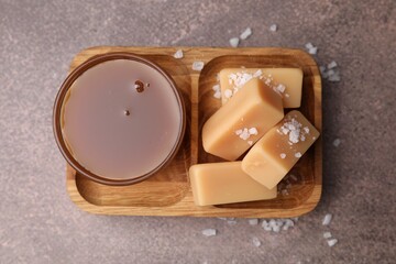 Yummy caramel candies, sauce and sea salt on brown table, top view