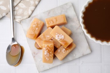Delicious candies with sea salt and caramel sauce on white tiled table, flat lay
