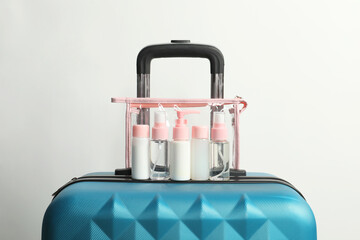 Cosmetic travel kit in plastic bag on suitcase against light background