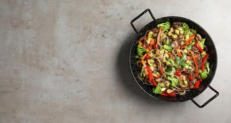 Stir-fry. Tasty noodles with meat and vegetables in wok on grey textured table, top view. Space for text