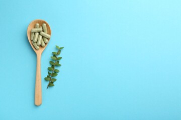 Vitamin capsules in spoon and green branch on light blue background, flat lay. Space for text