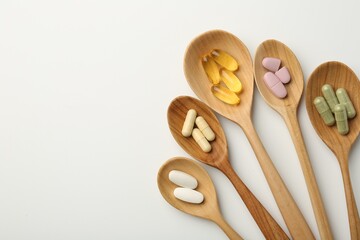 Vitamin capsules in wooden spoons on white background, flat lay. Space for text