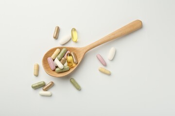 Different vitamin capsules in spoon on white background, top view