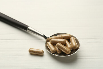 Vitamin capsules in spoon on white wooden table, closeup