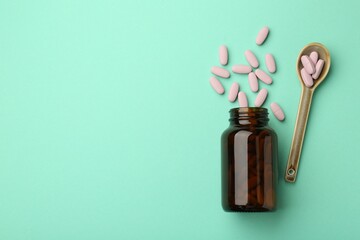 Vitamin pills, bottle and spoon on mint color background, flat lay. Space for text