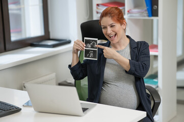 A pregnant woman shows a photo from an ultrasound scan of the fetus via video link in the office.