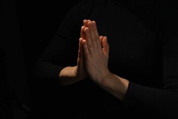 Religion. Christian woman praying on black background, closeup