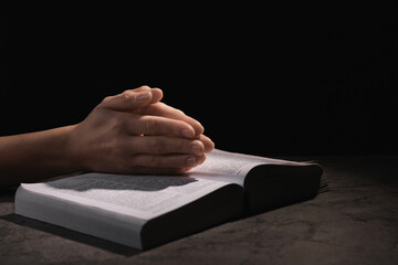 Religion. Christian woman praying over Bible at table against black background, closeup. Space for...