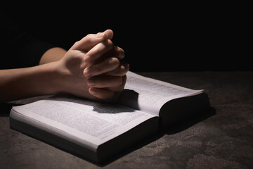 Religion. Christian woman praying over Bible at table against black background, closeup. Space for...