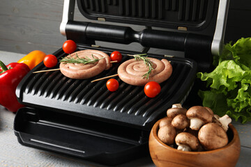 Electric grill with homemade sausages, rosemary and vegetables on rustic wooden table