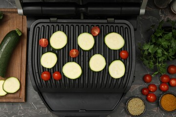 Electric grill with vegetables and spices on black marble table, flat lay