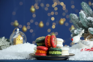 Different decorated Christmas macarons on blue table with artificial snow against blurred lights