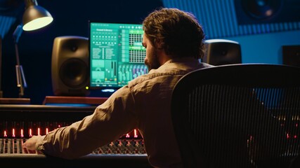 Sound designer mixing and mastering tracks on audio console in control room, using daw software on...
