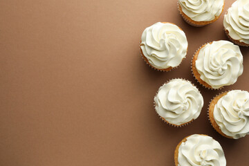 Tasty vanilla cupcakes with cream on dark beige background, top view. Space for text